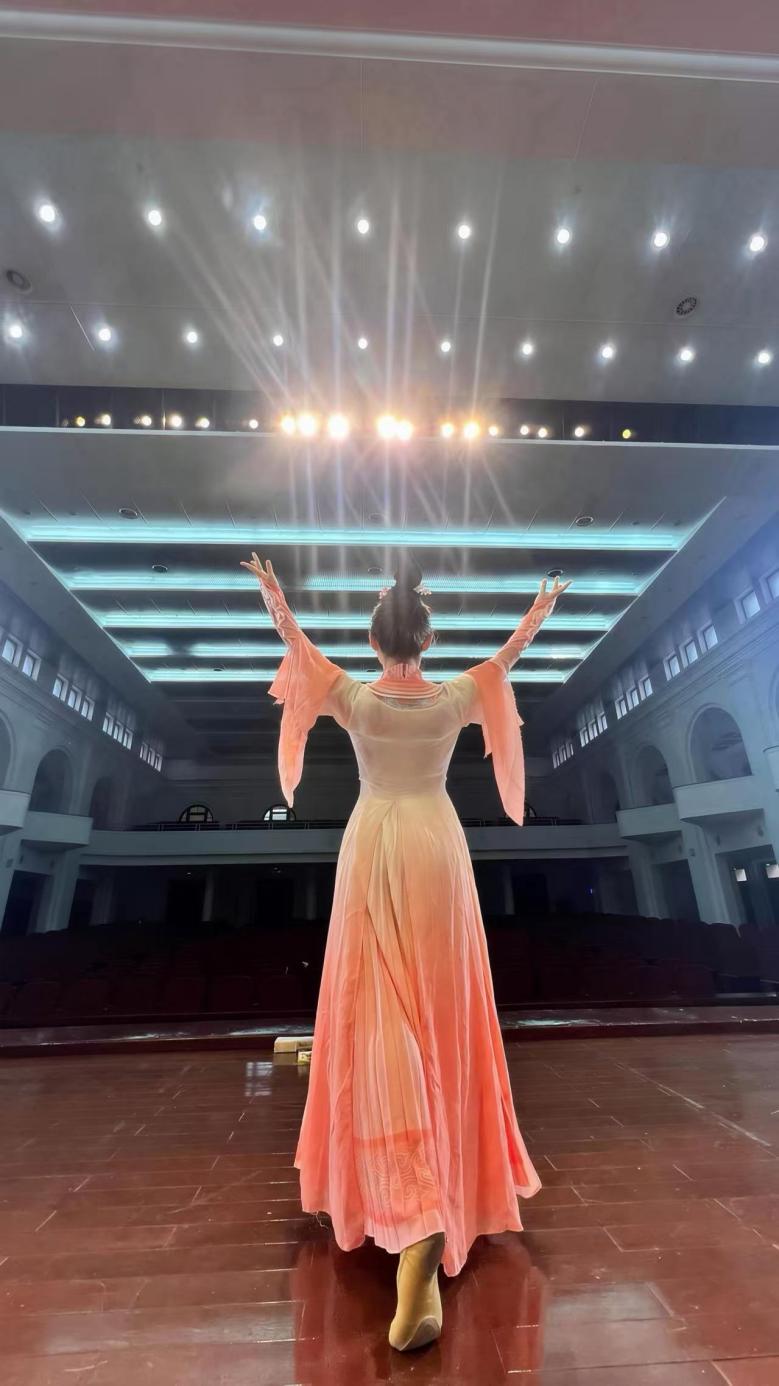 才艺:欧阳义莉在新会人民会堂的舞台上,背对镜头张开双臂,在聚光灯下进行舞蹈排练